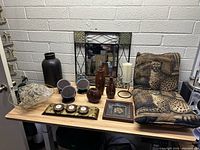 Full view of assorted home decor items arranged on table including vases, mirror, cushion, candle holders, framed artwork, and decorative bowl