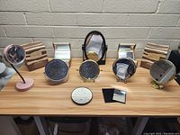 Photo showing the full lot of 9 vintage mirrors arranged on a wood table against a brick wall, including oval, round, and compact mirrors in various metal and plastic frames.