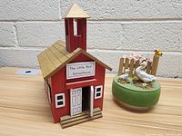 Photo of two vintage music boxes: a red schoolhouse and a green base with duck figures