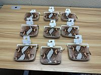 Top view of 10 snake print purses arranged in two rows on a wooden surface, showing front side with brand tags and zipper pull.