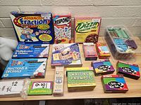 Photo showing the full assortment of math and homeschool educational games and flashcards arranged on a table, including playable card games, boxed games, flashcards, and plastic math manipulatives.