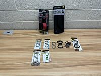 Photo shows eight Nite Ize gear/accessory items arranged on wooden desk in front of a white wall. Items include two packaged products and six loose clips and carabiners.