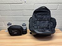 Photo showing the hiking backpack, waist pouch with two water bottles, all placed on a wooden table against a light gray brick wall.