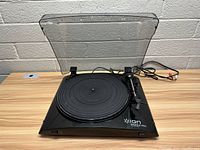 Front and angled view of the Ion Profile Pro USB turntable record player with raised dust cover and power cords visible.