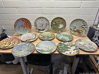 Overview of all 12 vintage Japanese decorative plates displayed on a table with varied natural and bird-themed designs