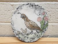 Front view of a round stone featuring a handpainted bird and chicks with flowers, signed 'St. Helen'.