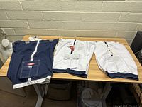Two pairs of men's swim trunks laid flat on a table, one navy blue and one white, showing front and back
