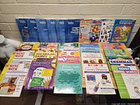 Photo showing a collection of teacher and homeschool workbooks on a table including language handbooks, math menus, vocabulary games, and grammar books.