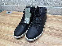 Front and side angle view of new black high-top shoes with size tag attached, showing clean details and lace-up closure.