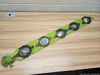 Five ornate oval picture frames mounted on a green fabric tapestry with tassels, set on a wooden table against a white brick wall.