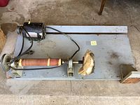 Overview of entire bench polisher unit showing motor, sanding drum wrapped in abrasive material, and buffing wheel mounted on wooden base.