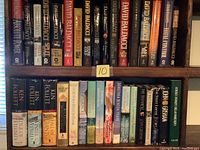 Books arranged on shelves showing spines with titles and authors mostly David Baldacci, plus Follett, Frank, Grisham