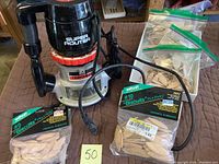 Overall view of Craftsman Super Router with cords and multiple bags of Woodcraft #10 wooden biscuits on table surface.
