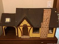 Front and side view of the antique wooden doll house showing exterior details including roof, chimney, door, and window openings.