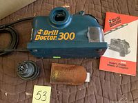 Drill Doctor 300 drill bit sharpener unit with power cord, manual, two sharpening chucks, and leather pouch.