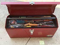 Open red metal toolbox showing variety of hand tools inside the top tray including screwdrivers, scissors, magnifying glass, and measuring tape.