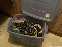 Blue plastic storage tote opened showing multiple Christmas string lights, extension cords, and a ceramic snowman inside.