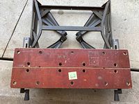 Top view of the folding work bench showing worn reddish wooden surface with multiple holes and label.