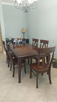 Photo showing the dark wood cherry dining table with six chairs arranged around it in a room with tiled floors. Table and chairs exhibit a polished finish with curved vertical slats on chair backs.