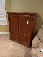 Front view of rectangular wooden entertainment center armoire, showing two paneled doors and top molding.
