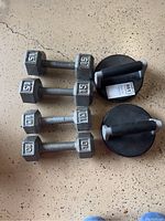 Two pairs of hex dumbbells (10 lbs and 15 lbs) placed side by side on a speckled floor alongside a pair of black and gray Perfect Pushup handles.