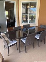 Photo showing the glass and metal rectangular outdoor dining table with three chairs on one side and three chairs visible overall.