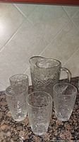 Four clear glass mugs and one clear glass pitcher with floral and fruit embossed patterns