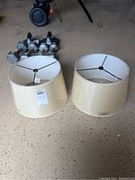 Two off-white drum lamp shades on concrete floor, showing the inside metal frames and outer fabric surface.