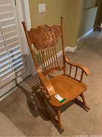 Front angled view of oak wood rocking chair showing carved backrest, spindled back supports, curved armrests, and seat contours.