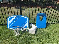 Plastic blue and white pool basketball backboard with hoop and net, white mounting arm, and 2 basketballs on grass near a fence.