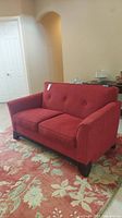 Front view of red loveseat showing three-button decorated backrest and two cushions on a floral rug.