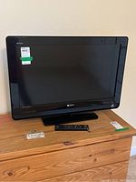 Front view of Sony Bravia 32" TV with remote on wooden chest, showing screen and branding.