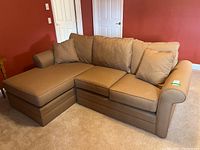 L-shaped brown upholstered sofa with three seat cushions, three back cushions, and two matching throw pillows, set in a carpeted room with red walls.