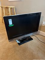 Front angle view of Vizio VX32L television on swivel stand with remote on the base, showing the full screen and surrounding casing.