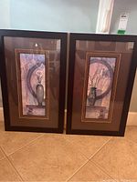 Two framed vertical floral vase art prints side by side standing on tile floor.