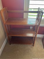 Front view of wooden 3 tier folding bookcase showing shelves and side slats with some scratches on shelves