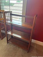 Photo of a 3-tier wooden bookcase with folding side panels, showing front and side views with visible wood grain and some scratches.
