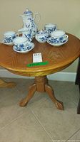 Round wood side table with pedestal legs, showing table top with scratches and wood grain.