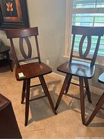 Two matching wooden swivel stools with dark brown finish and oval cutout backrest design shown from a frontal angle.
