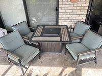 Full view of square fire pit table and four chairs on tiled patio