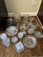 Full lot view of assorted pressed glass and cut crystal pieces on wooden floor.