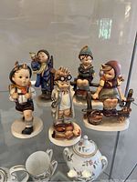 Five Hummel figurines grouped on display shelf