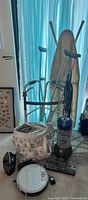 Ironing board, walker, crutches, Dyson upright vacuum, tote bag, and smaller vacuum attachment on carpeted floor.