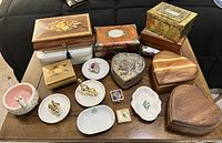 Overview photo showing assortment of different empty jewelry boxes, ring holders, small decorative and ceramic dishes arranged on a wooden table.