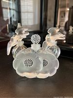 Three bottles: two swirl bodies with bird stoppers and one floral disc bottle with bubble stopper, front view