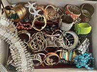 Velvet-lined top tier of jewelry chest containing assorted metal-tone bangles and bracelets