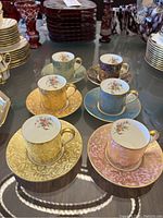 Five Minton Brocade demitasse cups and matching saucers in assorted colors displayed on a table with other dishware around.