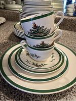 Stacked set of Spode Christmas Tree cups and plates with green borders and Christmas tree decoration, showing condition including some chips on cup rims.