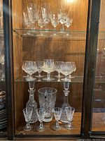 Three shelves of Waterford cut crystal in wood cabinet: top shelf wine glasses, middle dessert glasses and candy dish, bottom cordial glasses, decanters, vase