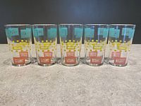 Front view showing all 5 Dominion Glass juice glasses with atomic era patterns in teal, yellow, and orange on clear glass.